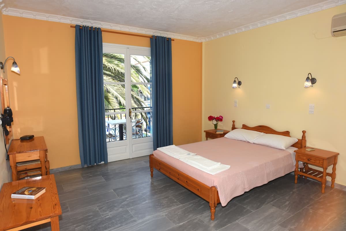 A bedroom with a bed, bedside tables, a nightstand, a window with curtains, a lamp, and a view of palm trees.
