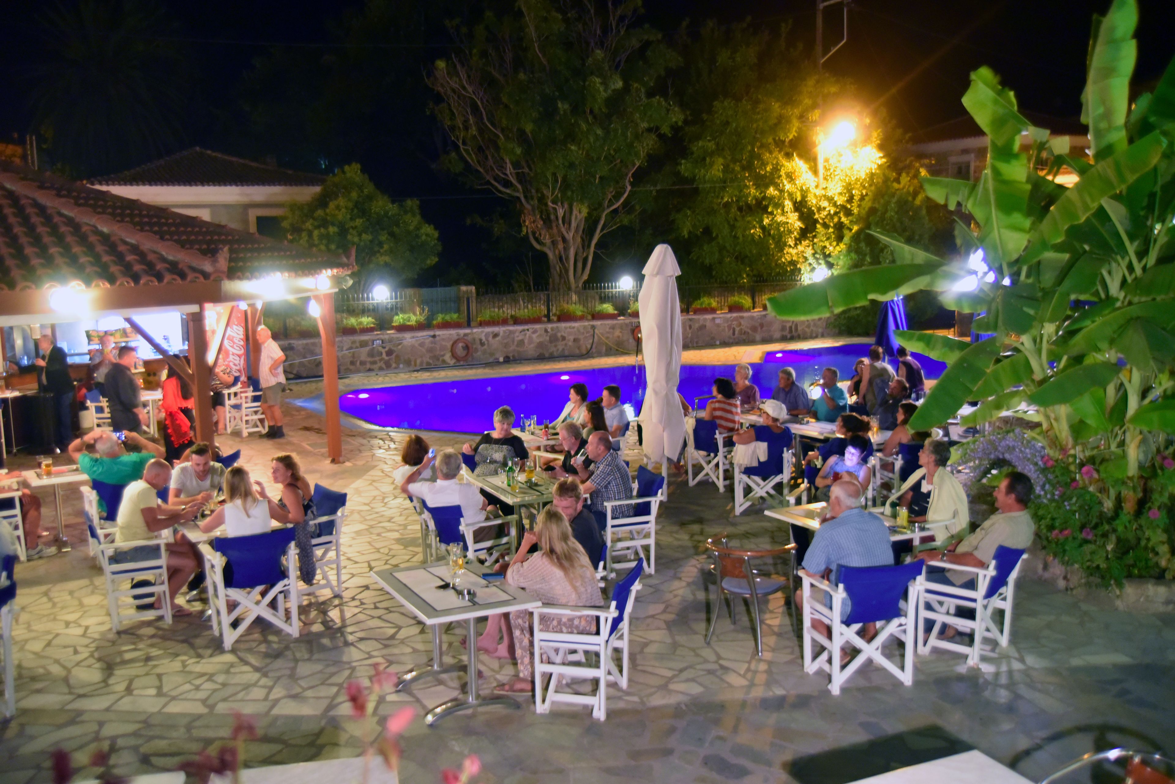 An outdoor dining area with tables and chairs, a pool, and a covered seating area.