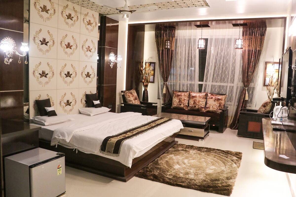 A modern bedroom with a large bed, a sofa, a small table, and a TV.