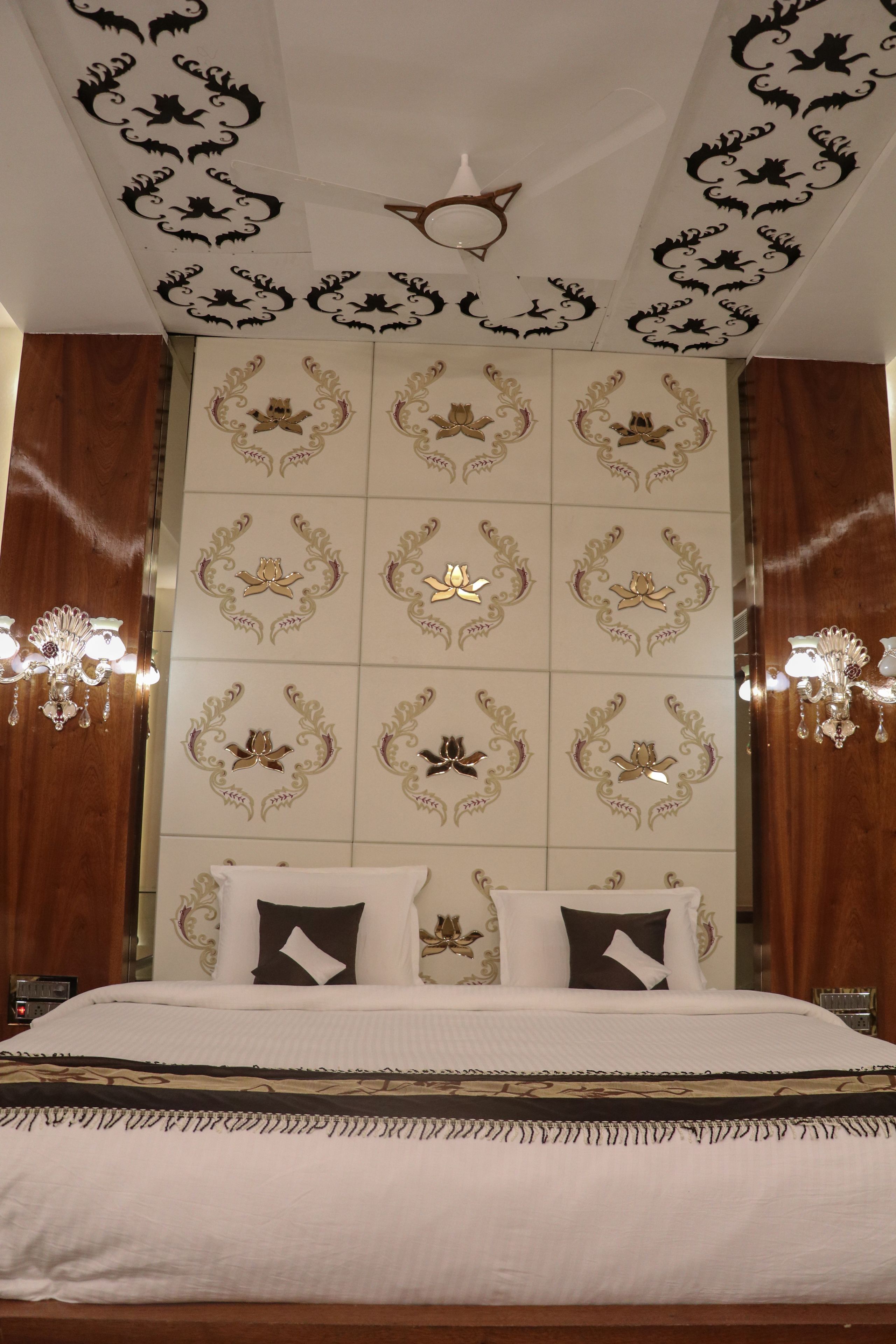 A hotel room with a large bed, ornate wall decorations, and two wall-mounted chandeliers.