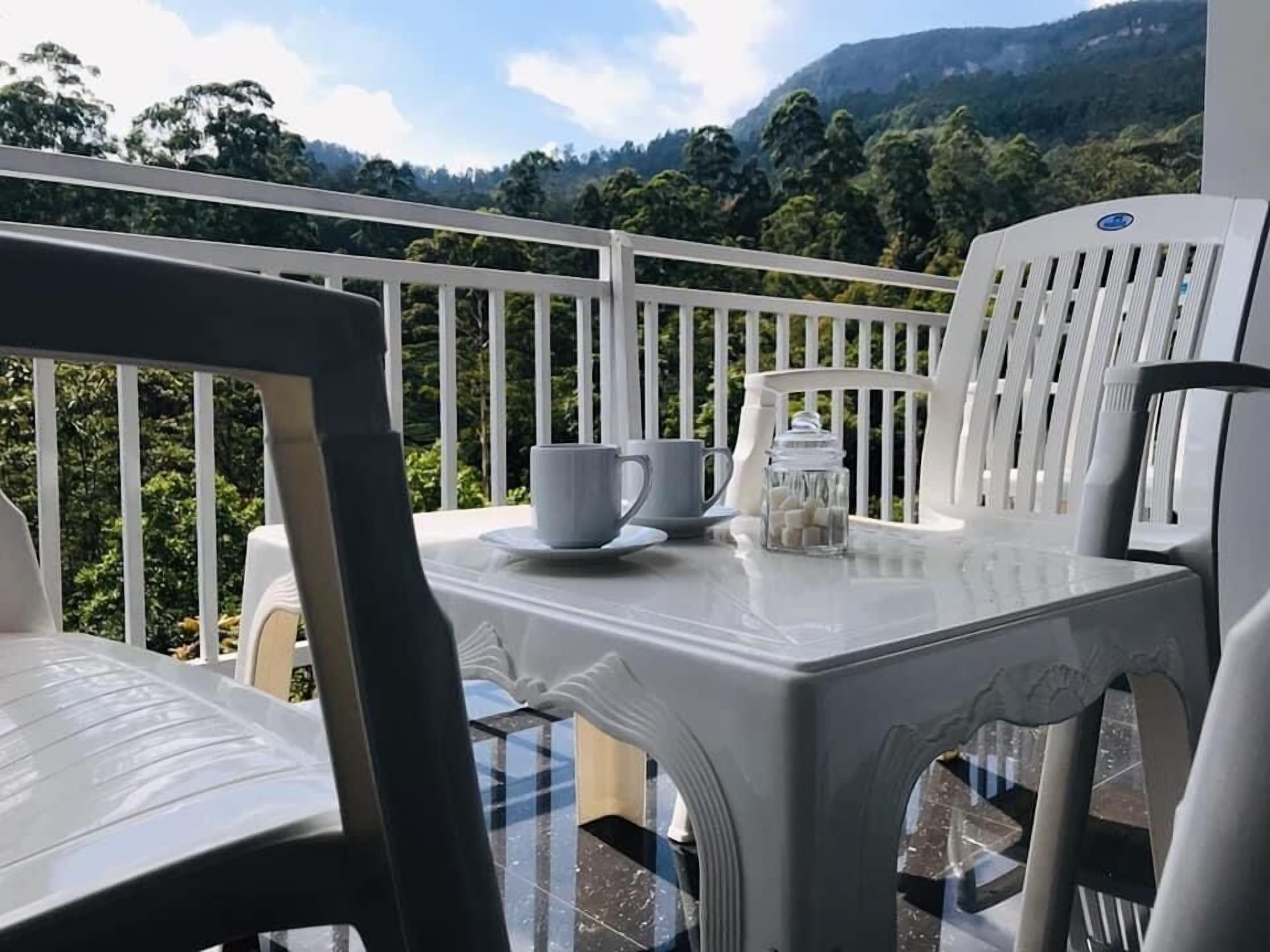 Een balkon met witte stoelen en een tafel, een kopje en een suikerpot.