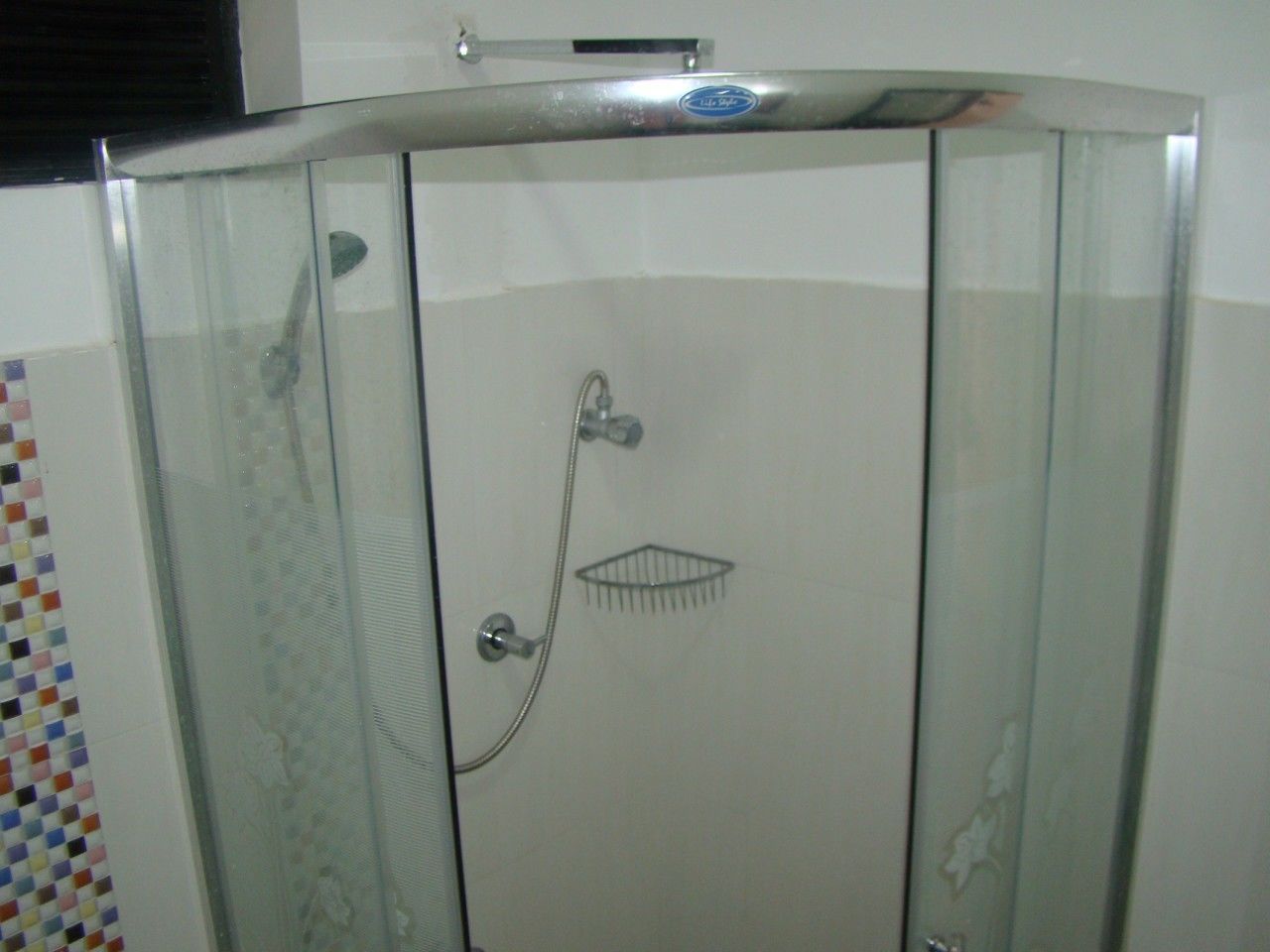 Ducha con cerramiento de vidrio, cabezal de ducha de mano y grifo empotrado.
