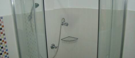Ducha con cerramiento de vidrio, cabezal de ducha de mano y grifo empotrado.