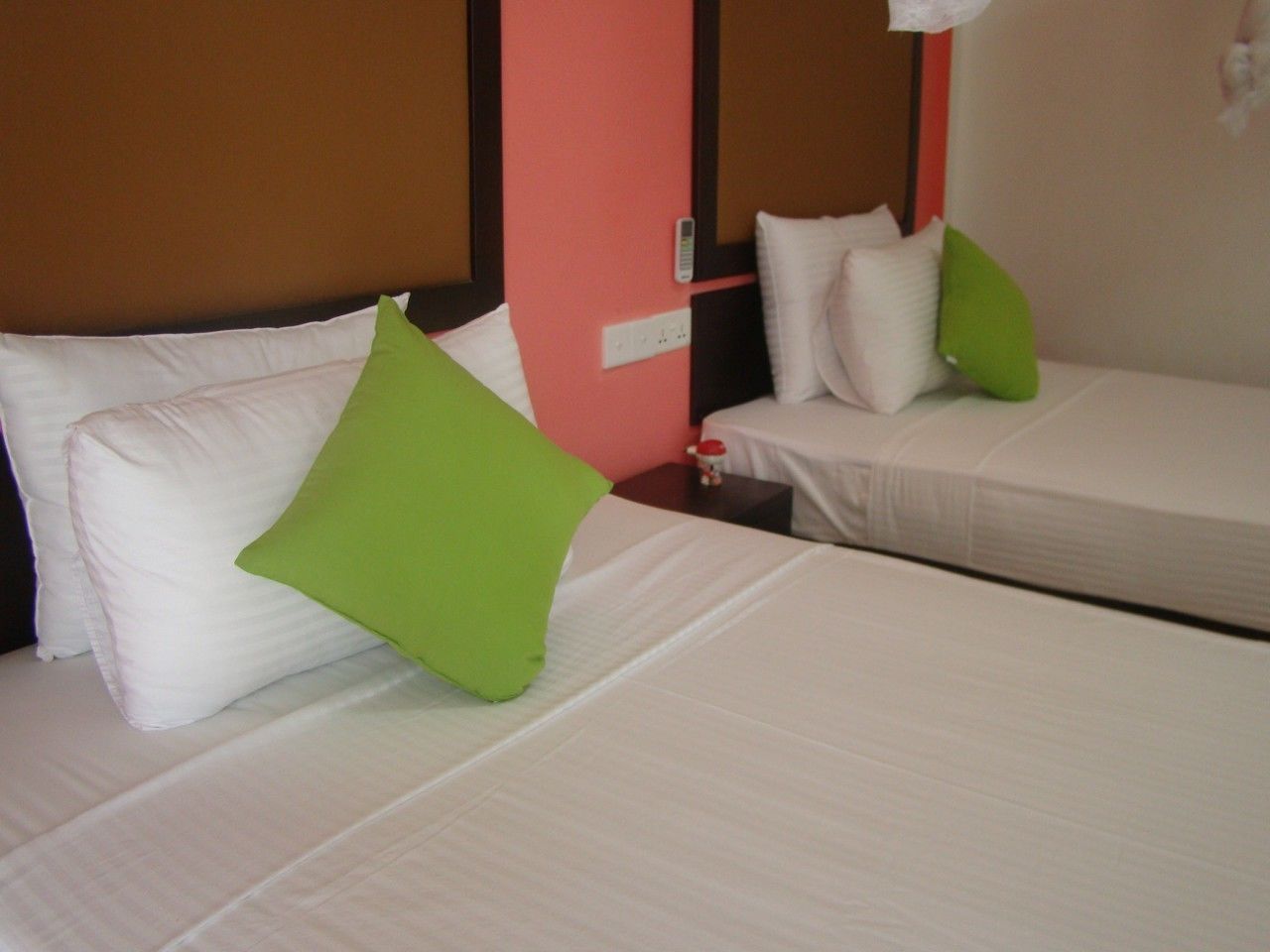 Two beds with white bedding and green pillows in a room with a brown headboard and a red accent wall.