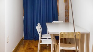 Ein kleiner Raum mit einem weißen Tisch und Stühlen, einem blauen Vorhang und einer Stehlampe.