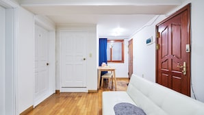 Ein Flur mit Holzboden, weißen Wänden, einer weißen Tür, einer Holztür und einem weißen Sofa mit grauer Decke.