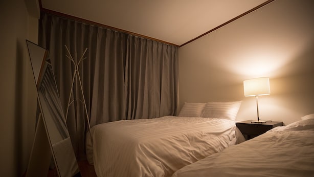 Ein Hotelzimmer mit zwei Betten, einem Nachttisch mit Lampe, einem Spiegel und einem Fenster mit Vorhängen.