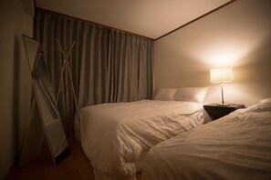 A hotel room with two beds, a nightstand with a lamp, a mirror, and a window with curtains. - Myeongdong Residence (Seoul)