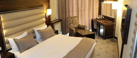 Una habitación de hotel con una cama grande, una silla, un escritorio y un espejo.