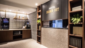 Un espace d’accueil d’hôtel au design moderne, avec un mur en briques, des étagères en bois remplies de livres et un écran numérique affichant des informations sur les chambres.