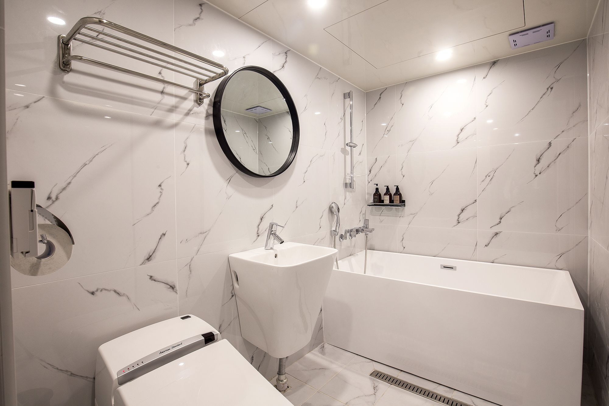 Uma casa de banho moderna com uma pia branca, um espelho, um chuveiro e uma sanita.