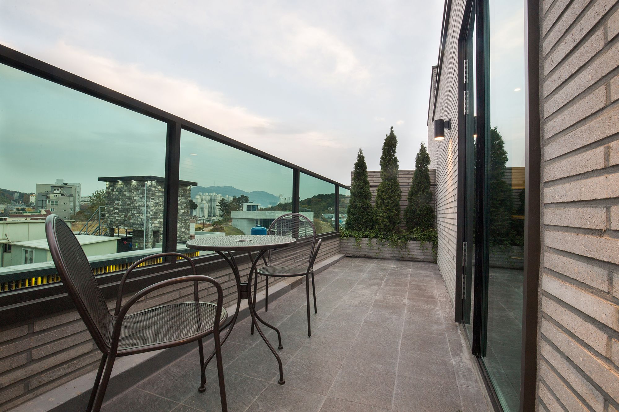 Un balcón con vistas a edificios y árboles, amueblado con sillas de metal y una mesa.