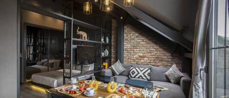 Un comedor moderno con una mesa de madera dispuesta para una comida, un sofá con cojines estampados y una pared de ladrillo al fondo.