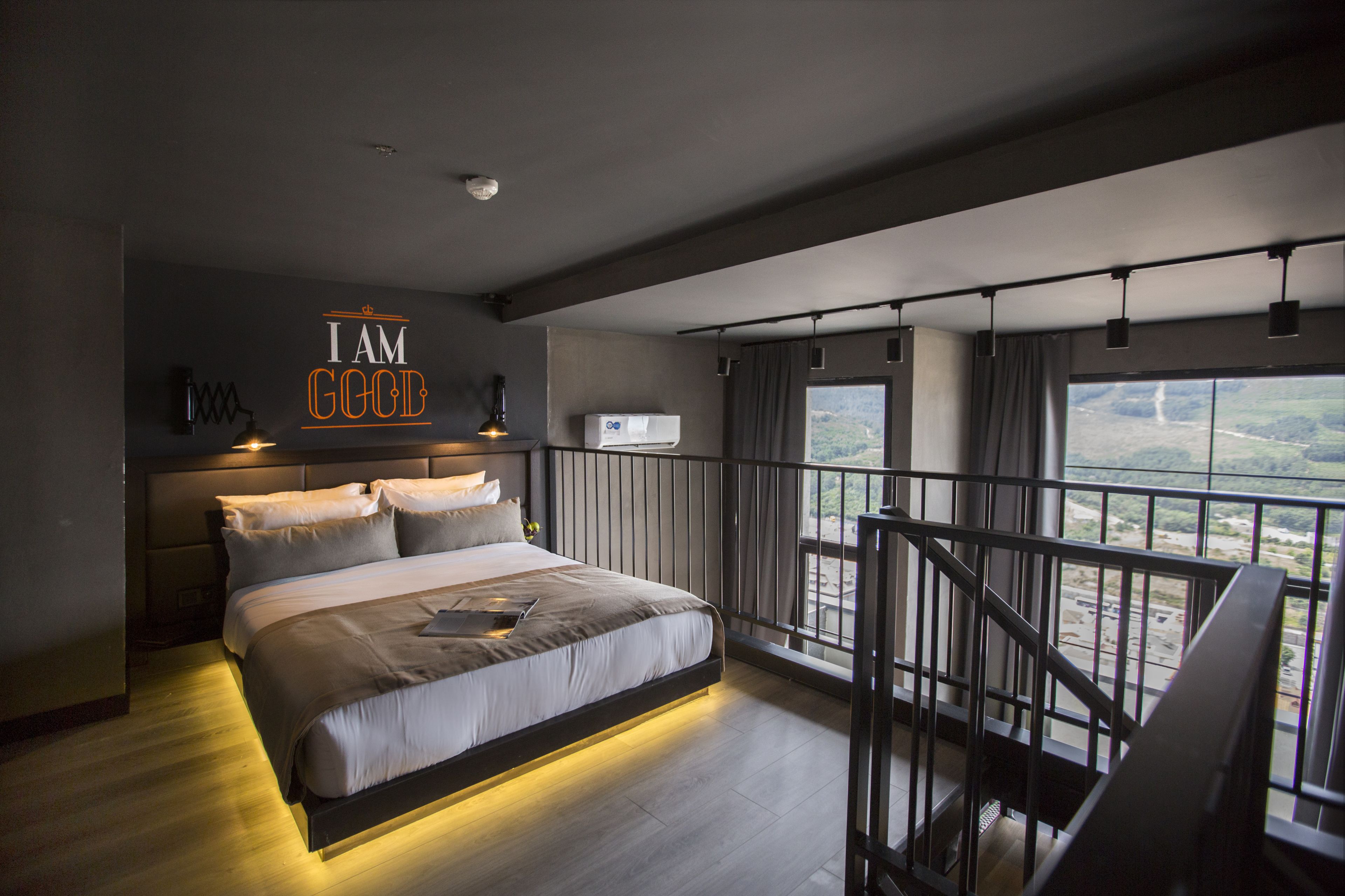 A modern bedroom with a large bed, a view of the outdoors, and a balcony with a railing.