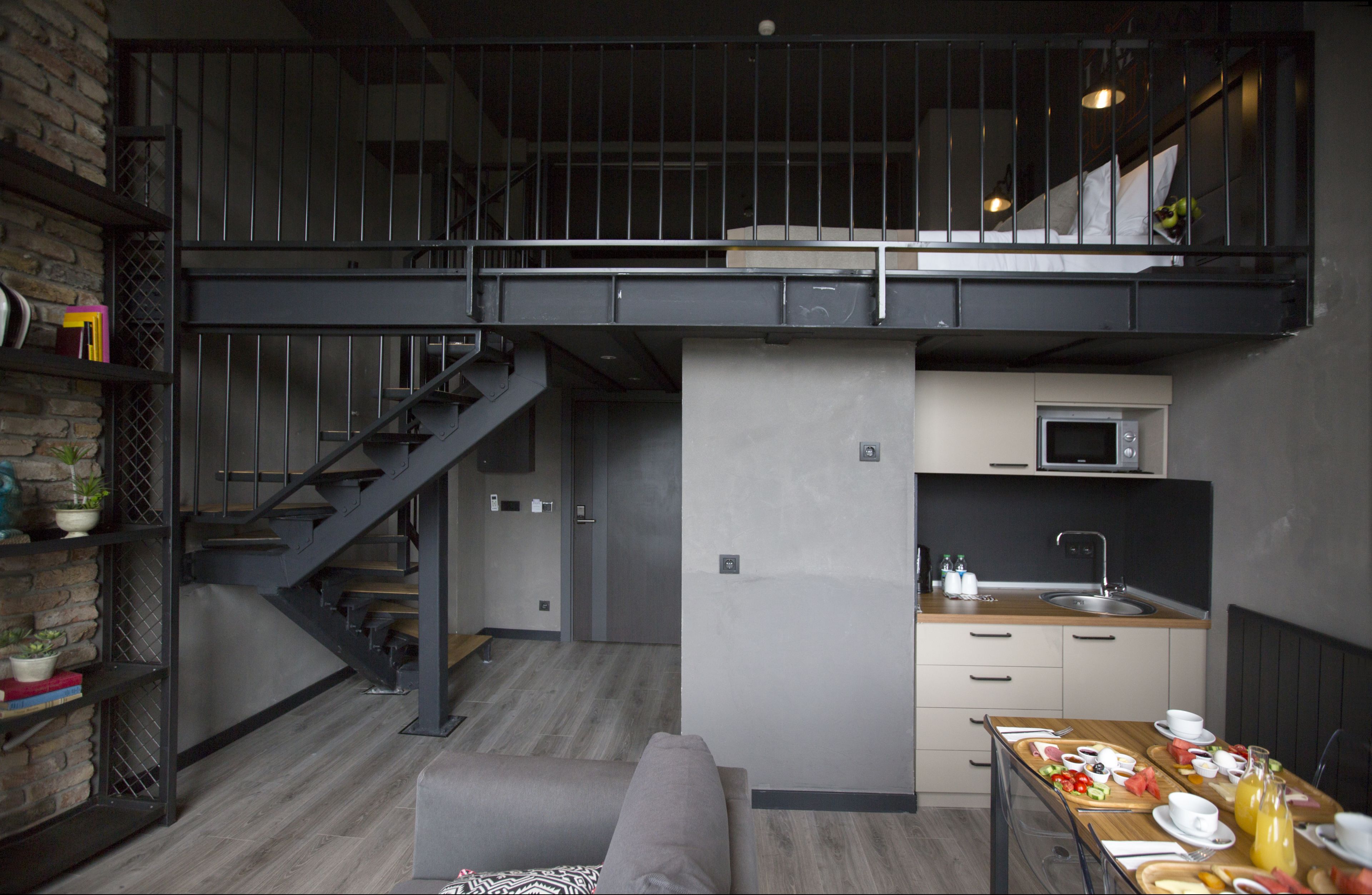A loft-style bedroom with a mezzanine, a kitchen area, and a staircase.