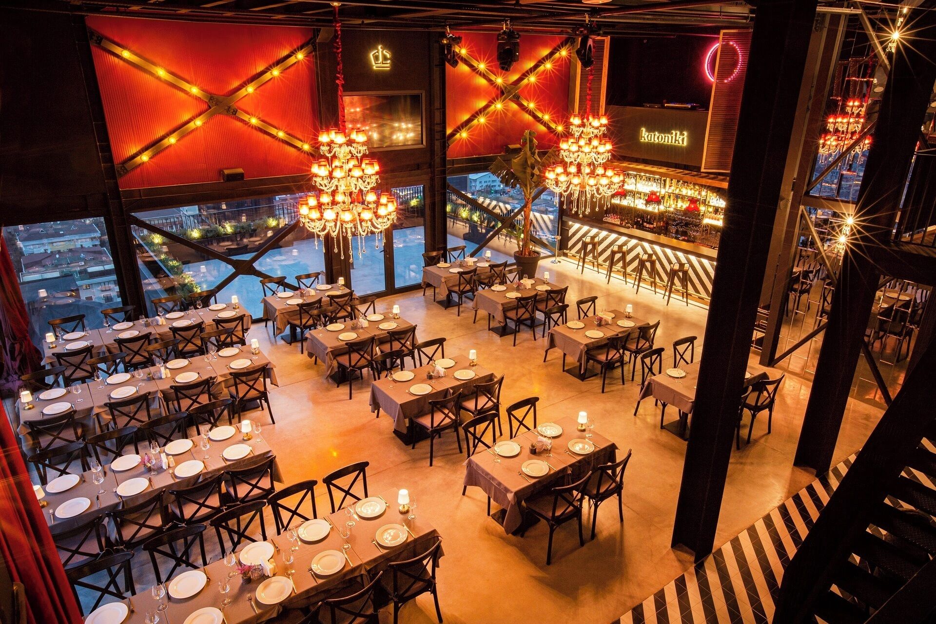 A restaurant with multiple dining tables set for guests, a bar area, and a view of the cityscape through large windows.