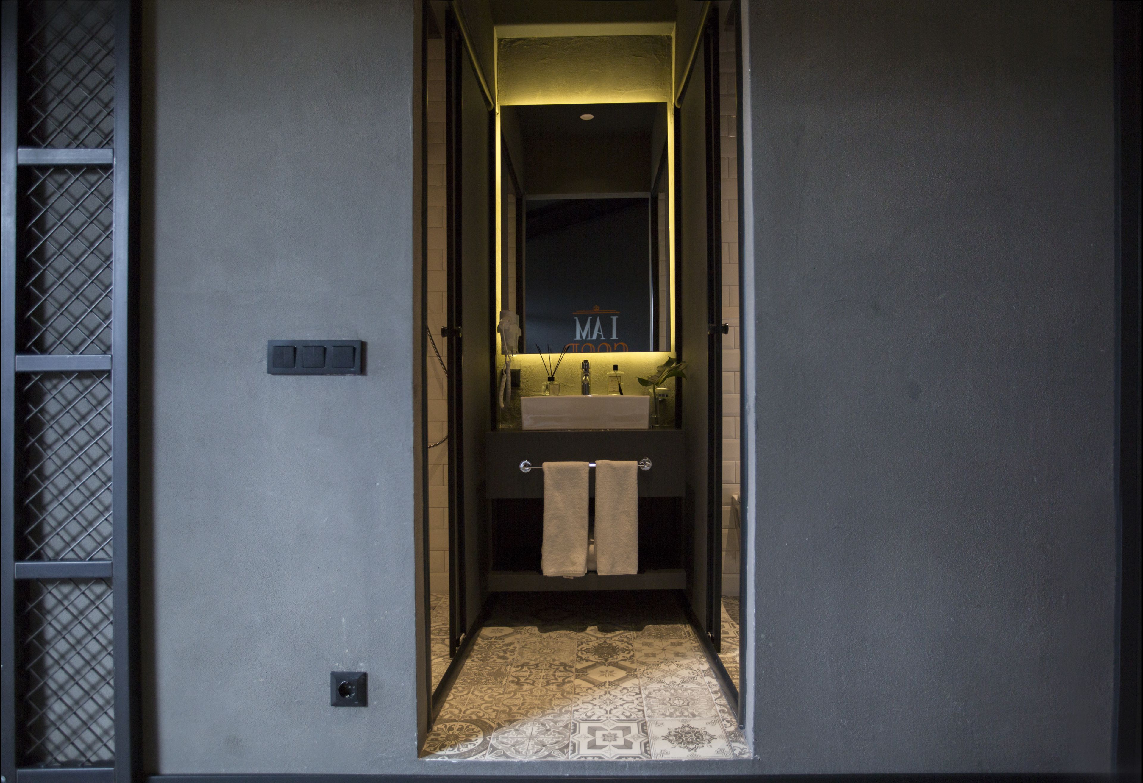 Un couloir étroit mène à une salle de bain équipée d’un lavabo et d’un porte-serviettes.