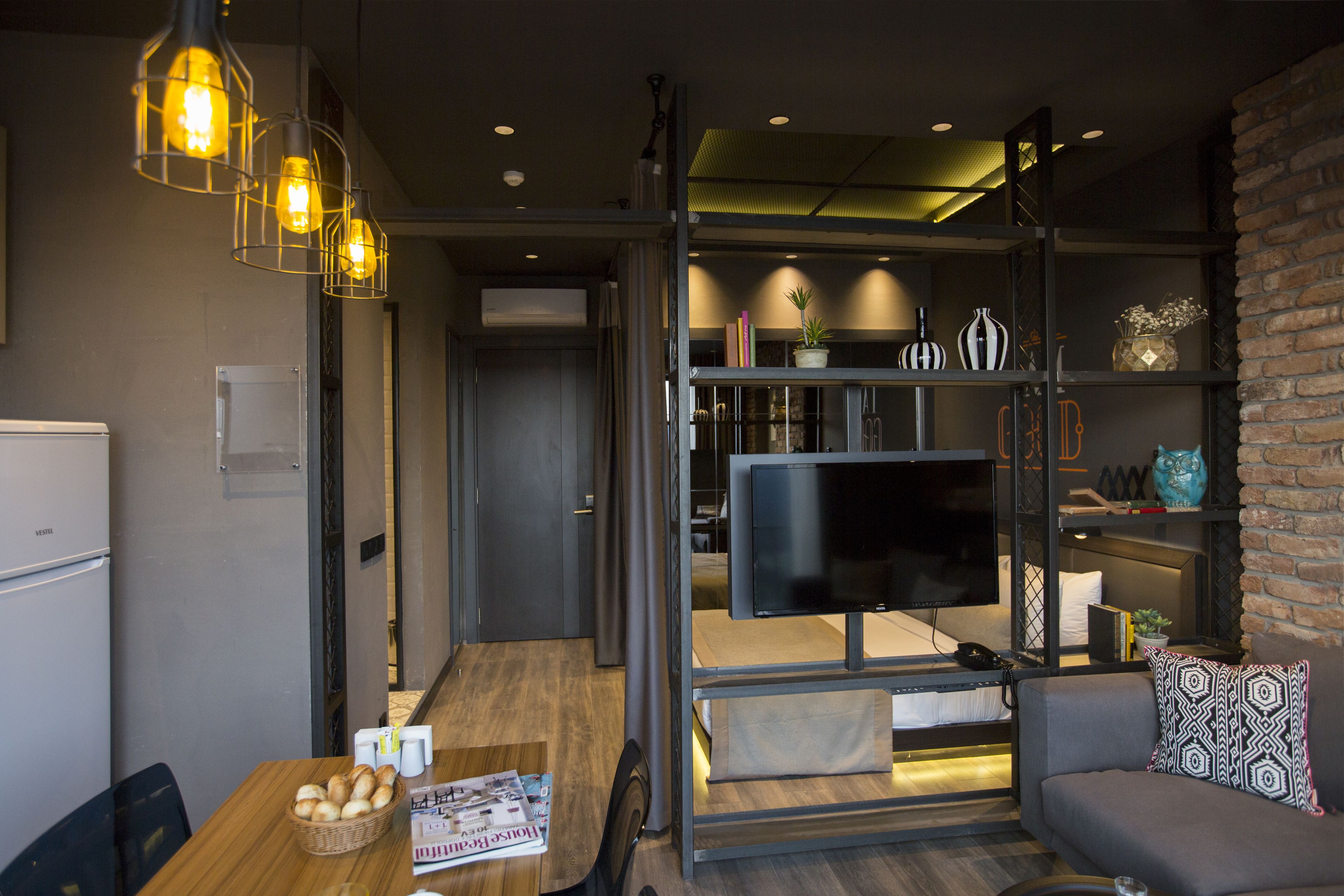 A modern living room with a sofa, a dining table with a basket of bread, a TV on a stand, and a brick wall.