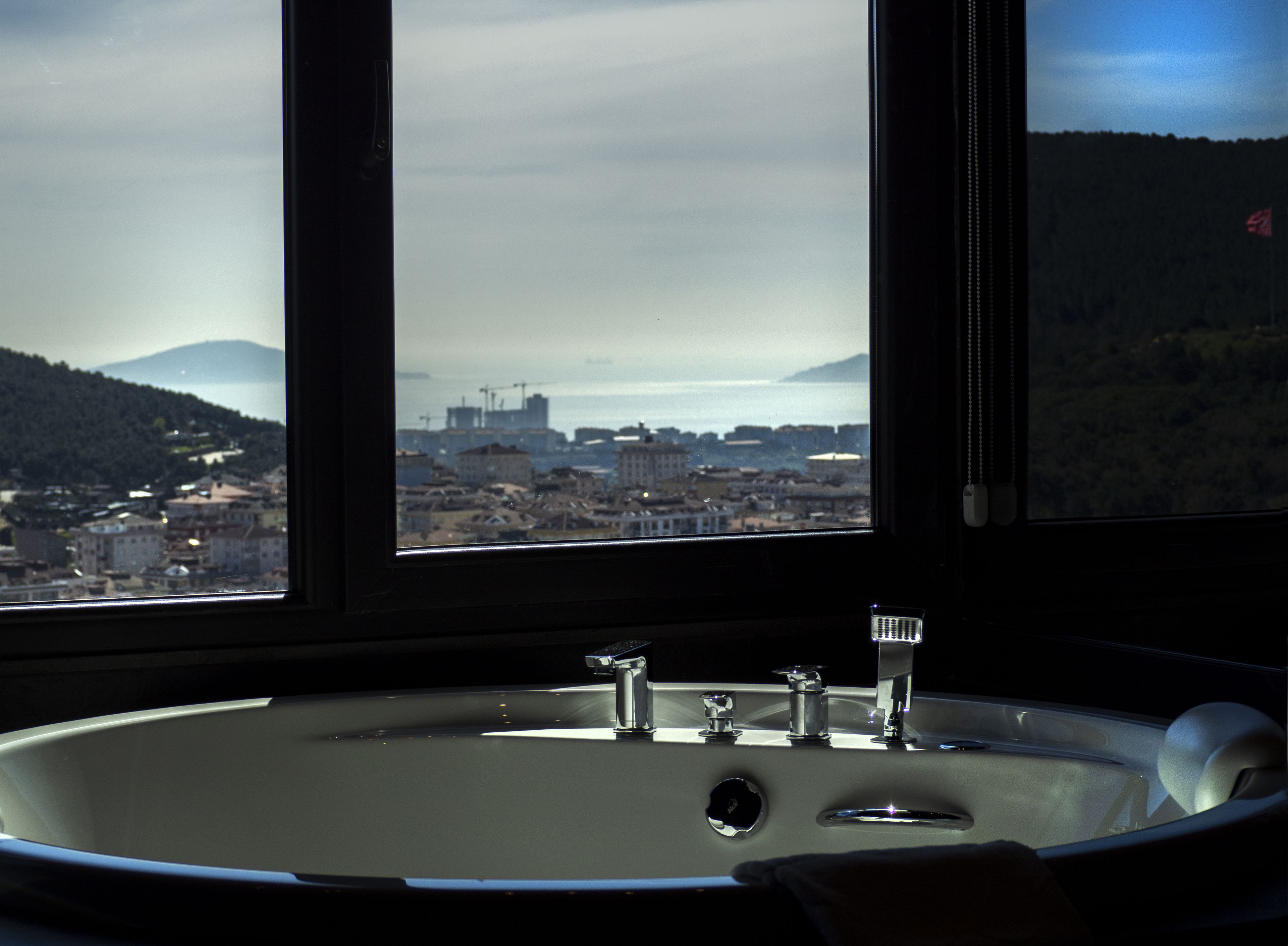 Un baño con una bañera grande, una ventana que ofrece vistas a la ciudad y montañas.