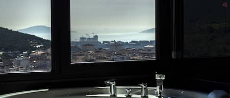 A bathroom with a large bathtub, a window with a view of a cityscape and mountains.
