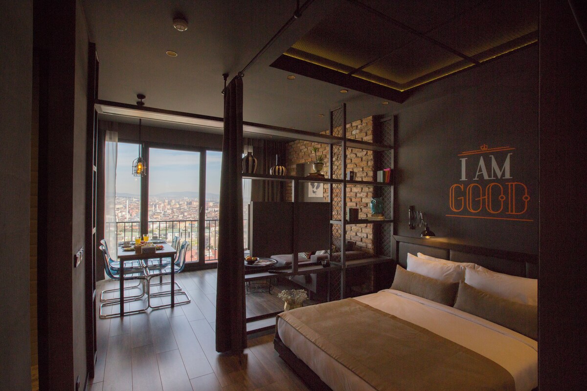 A modern bedroom with a large bed, a desk, and a view of the city.