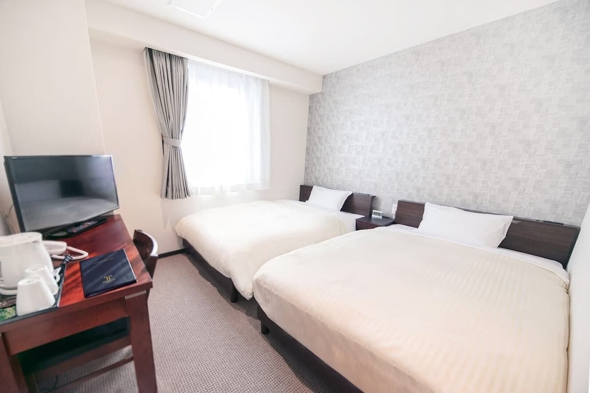 A hotel room with two beds, a desk with a television, and a window with curtains.