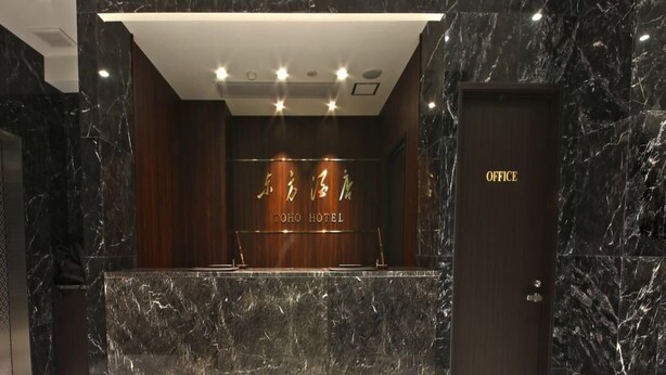 A reception desk with a marble countertop and a wooden panel backdrop displaying the hotel name. - Toho Hotel (Osaka)