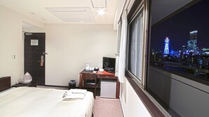 A hotel room with a bed, desk, and a view of a cityscape at night. - Toho Hotel (Osaka)