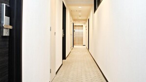 A narrow hallway with a patterned carpet, white walls, and a door on the left. - Toho Hotel (Osaka)