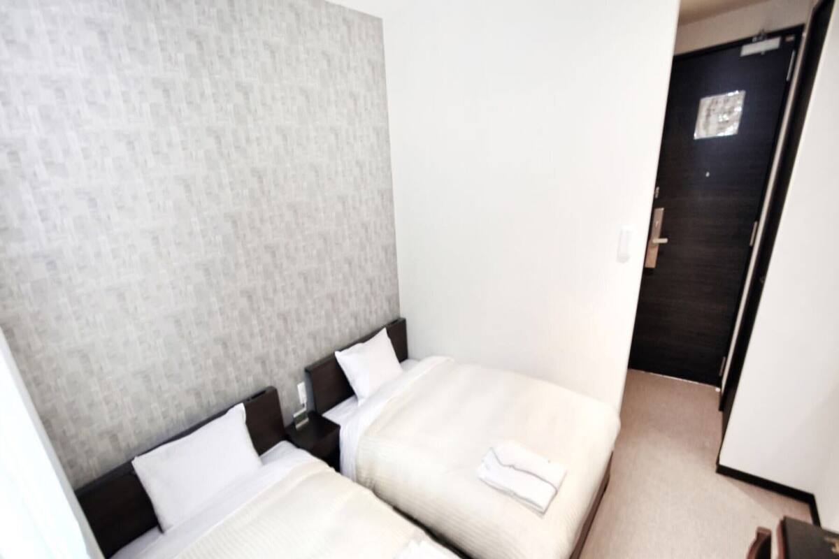 A hotel room with two single beds, a grey textured headboard, white linens, and a wooden desk with a chair.