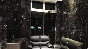 A modern interior with black leather sofas, a marble wall, and a glass elevator. - Toho Hotel (Osaka)
