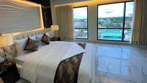 A modern hotel room with a large bed, a ceiling fan, and a city view through large windows.