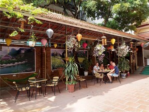 Un café en plein air avec des chaises et des tables en osier, entouré de plantes en pot et de lanternes suspendues.