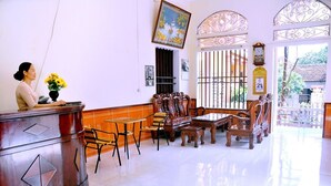 A reception area with a wooden reception desk, several chairs, a piano, and a large window with decorative ironwork. - Tam Coc Family Hotel Ninh Binh (Nam Hoa Lu)