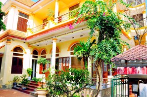 Un bâtiment à deux étages doté d’un balcon, de plantes en pot et d’un petit espace jardin.