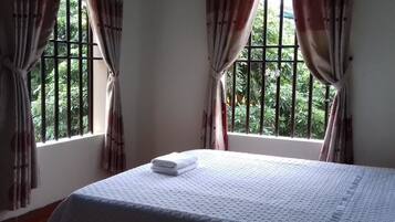 A room with a bed, curtains, and a window with a view of greenery.
