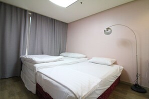 Una habitación de hotel con cama, escritorio, silla, lámpara y ventana con cortinas.