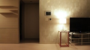 Ein Zimmer mit einem Holzschrank, einem an der Wand befestigten Thermostat, einem Fernseher auf einem weißen Schrank und einem Tisch mit rotem Rahmen.