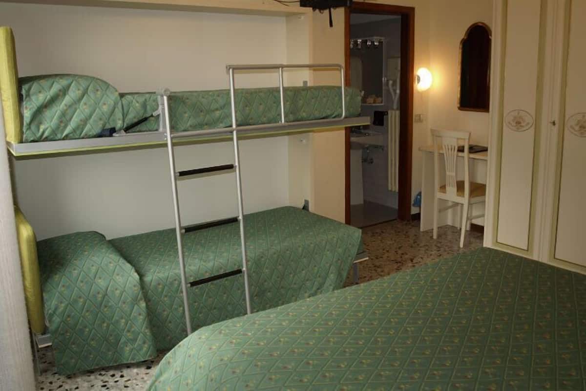 A dormitory room with bunk beds, a desk, and a chair.