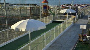 A beachside walkway with umbrellas and a green artificial turf area. - Hotel Pensione Elena (Misano Adriatico)