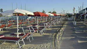 A beach with rows of sun loungers and umbrellas, a sandy walkway, and a clear sky. - Hotel Pensione Elena (Misano Adriatico)