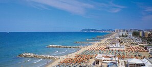 A beach with rows of umbrellas and beach chairs, a rocky breakwater, and buildings in the background. - Hotel Pensione Elena (Misano Adriatico)