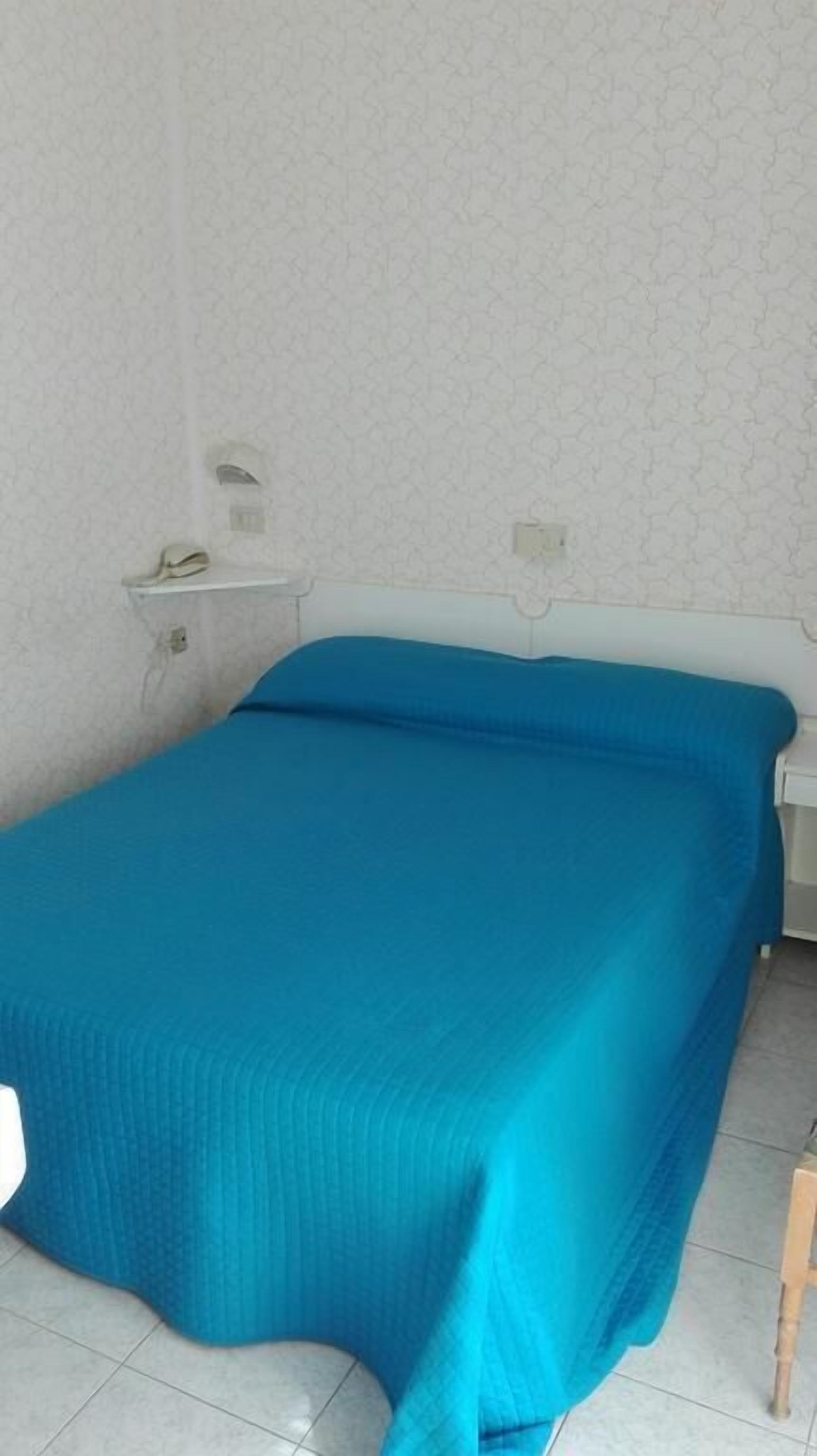 A single bed with a blue bedspread in a room with white walls and a patterned wallpaper.