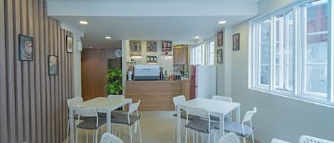 Un comedor moderno con mesas y sillas blancas, un revestimiento de pared de madera y una cocina al fondo.