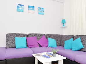 A modern living room with a purple sofa, teal cushions, and a small table with a magazine and a plant.