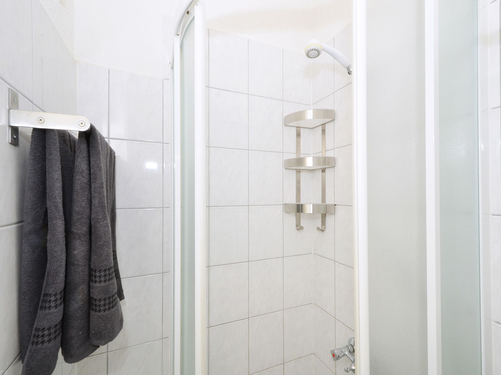 A shower with a glass door, a towel rack with towels, and a showerhead.