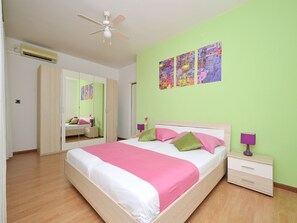 A bedroom with a bed, bedside tables, a wardrobe, a ceiling fan, and a wall with colorful artwork.