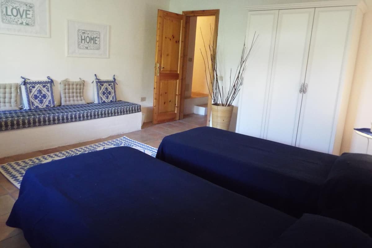 A room with two beds, a bench with cushions, a door, and a wall with framed pictures.