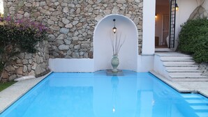 A swimming pool with a stone wall and a white archway. - Villa delle Rocce (Olbia)