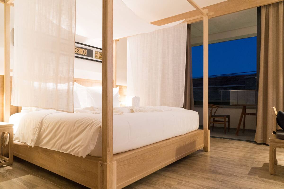 Un dormitorio moderno con una cama de madera con dosel, cortinas traslúcidas y vistas al exterior.